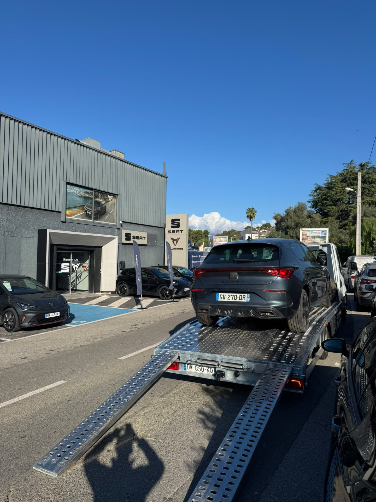 Camion plateau FAST DÉPANNAGE livrant une Cupra León grise chez un concessionnaire